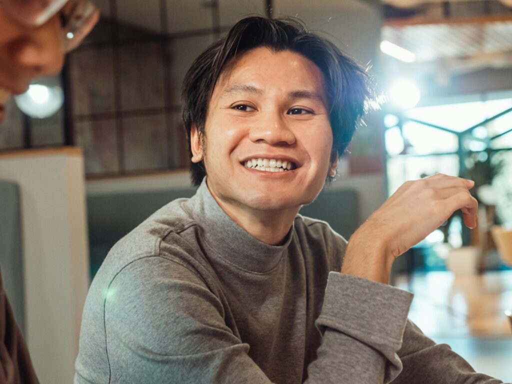 Close-up of a smiling Asian man wearing a sweater indoors.